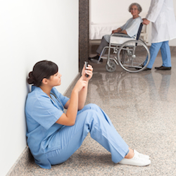 Nurse looking at her mobile phone while sitting in the hallway